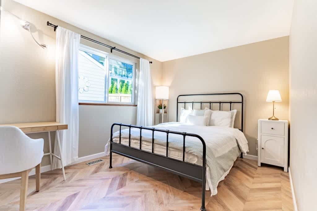 Pristine queen bed in a serene white room, with a cozy desk for productivity.