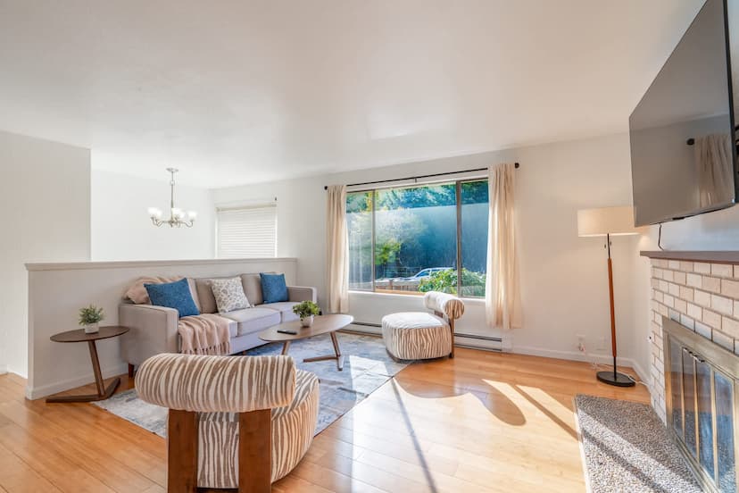 Bright and airy living room with a cozy fireplace, ample seating, and large windows offering a view of the outdoors.