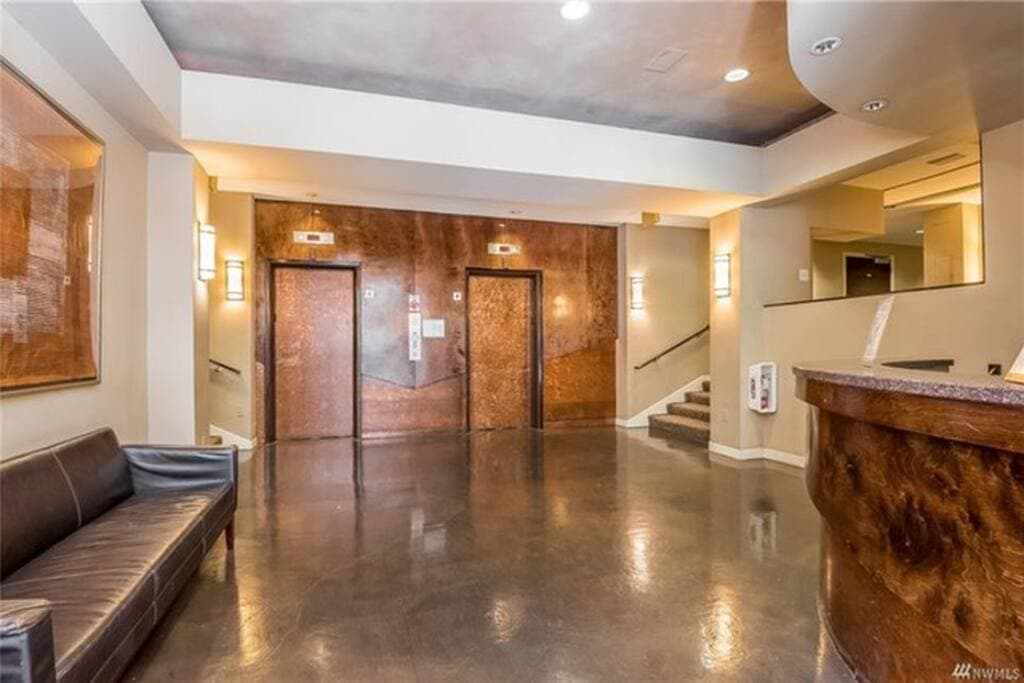 The entrance lobby features a sleek and modern design with polished floors, warm lighting, and two centrally located elevators.