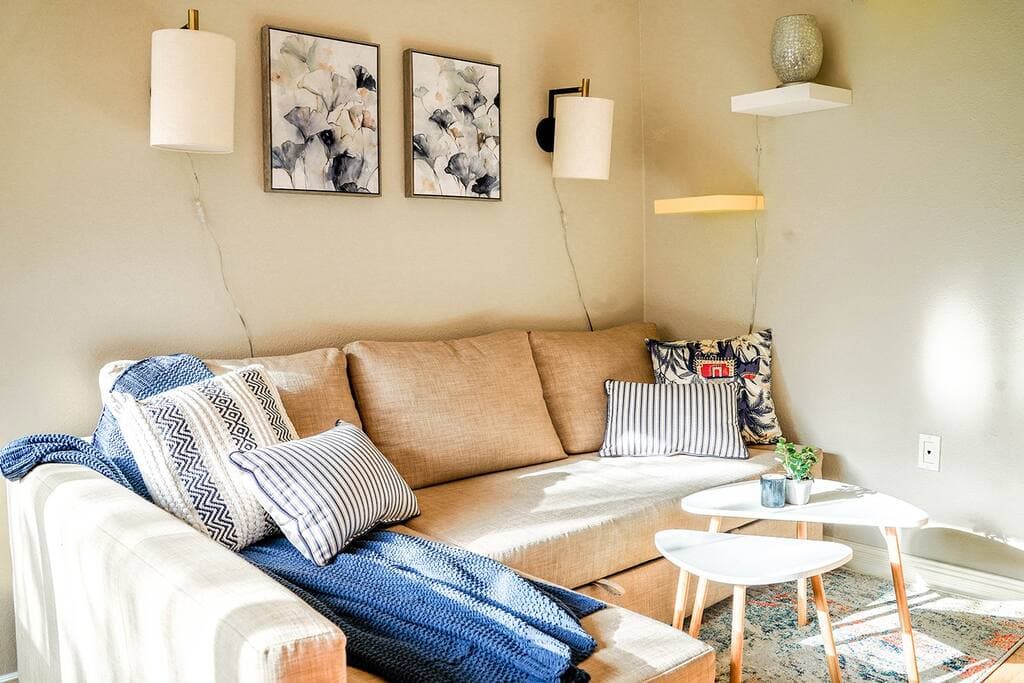 Relax in this cozy and stylish living room featuring a soft beige sectional, chic wall art, and warm natural light perfect for unwinding.