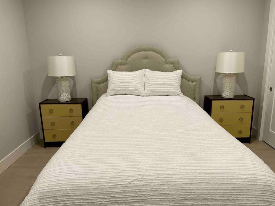 Inviting bedroom with a queen-sized bed and elegant scalloped headboard. Thoughtfully styled with matching nightstands and lamps to make any guest feel welcome.