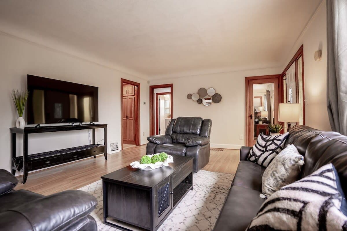 This cozy living room features modern leather seating, a sleek black coffee table, and a large flat-screen TV for entertainment. The space is enhanced with warm wooden accents, neutral tones, and decorative touches for a welcoming atmosphere.