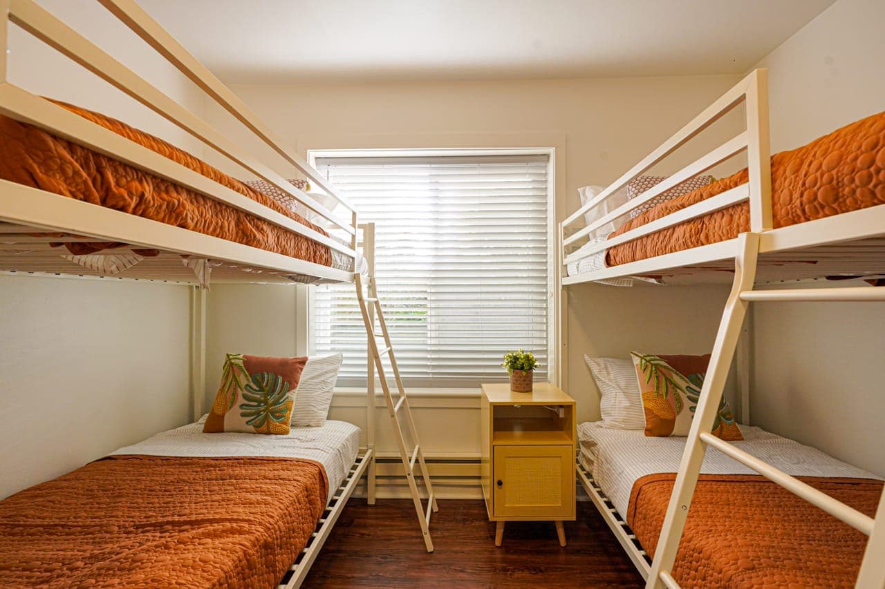 Cozy and bright bunk bedroom features two sturdy twin-over-twin bunk beds, comfortably sleeping four guests. With warm-toned bedding, leafy accent pillows, and natural light filtering through the blinds, it’s the perfect space for families or groups.