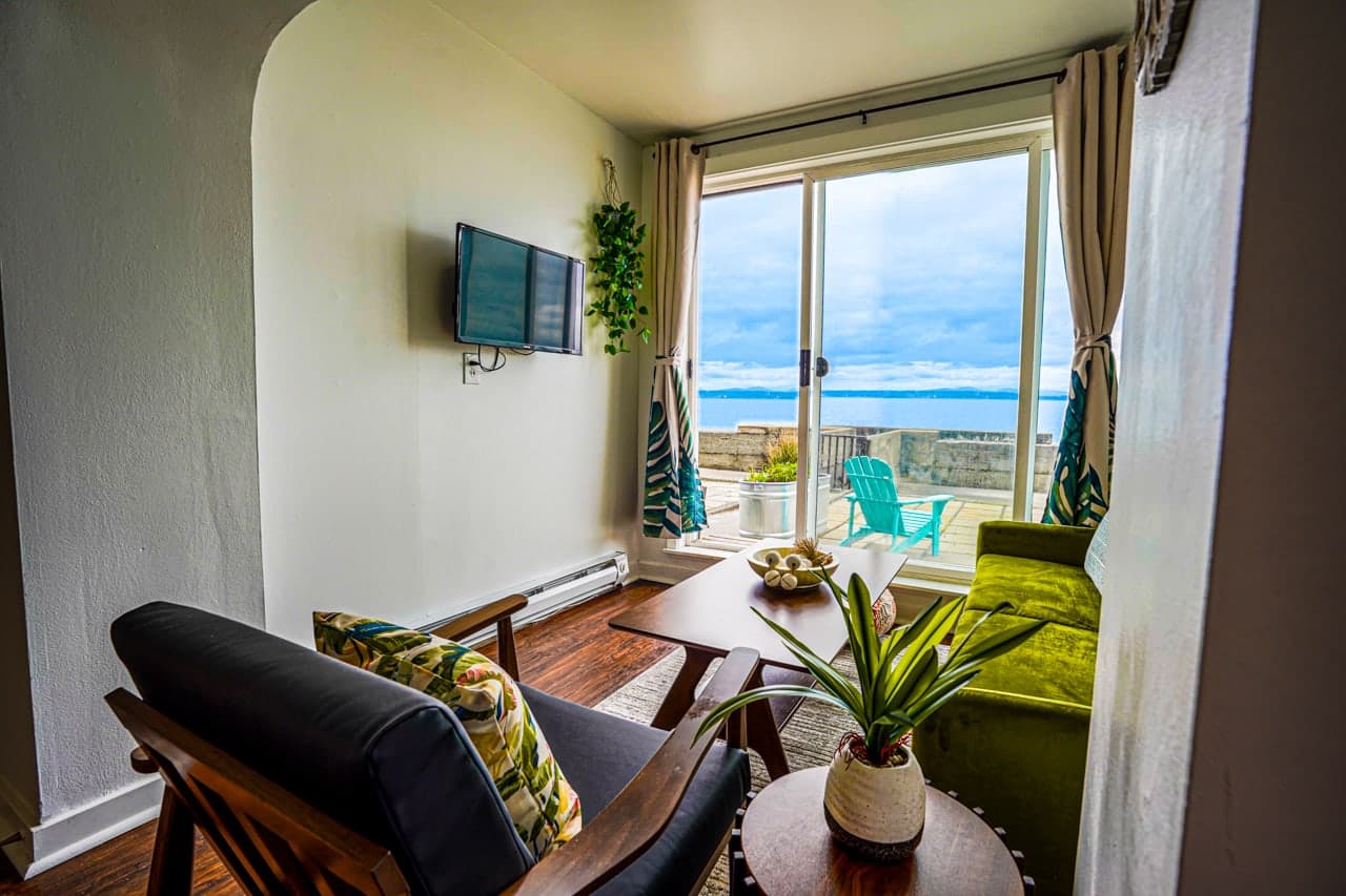 This is a bright and stylish waterfront living room with modern coastal décor. Enjoy stunning ocean views from the comfort of a vibrant green velvet sofa, just steps from a spacious seaside patio.