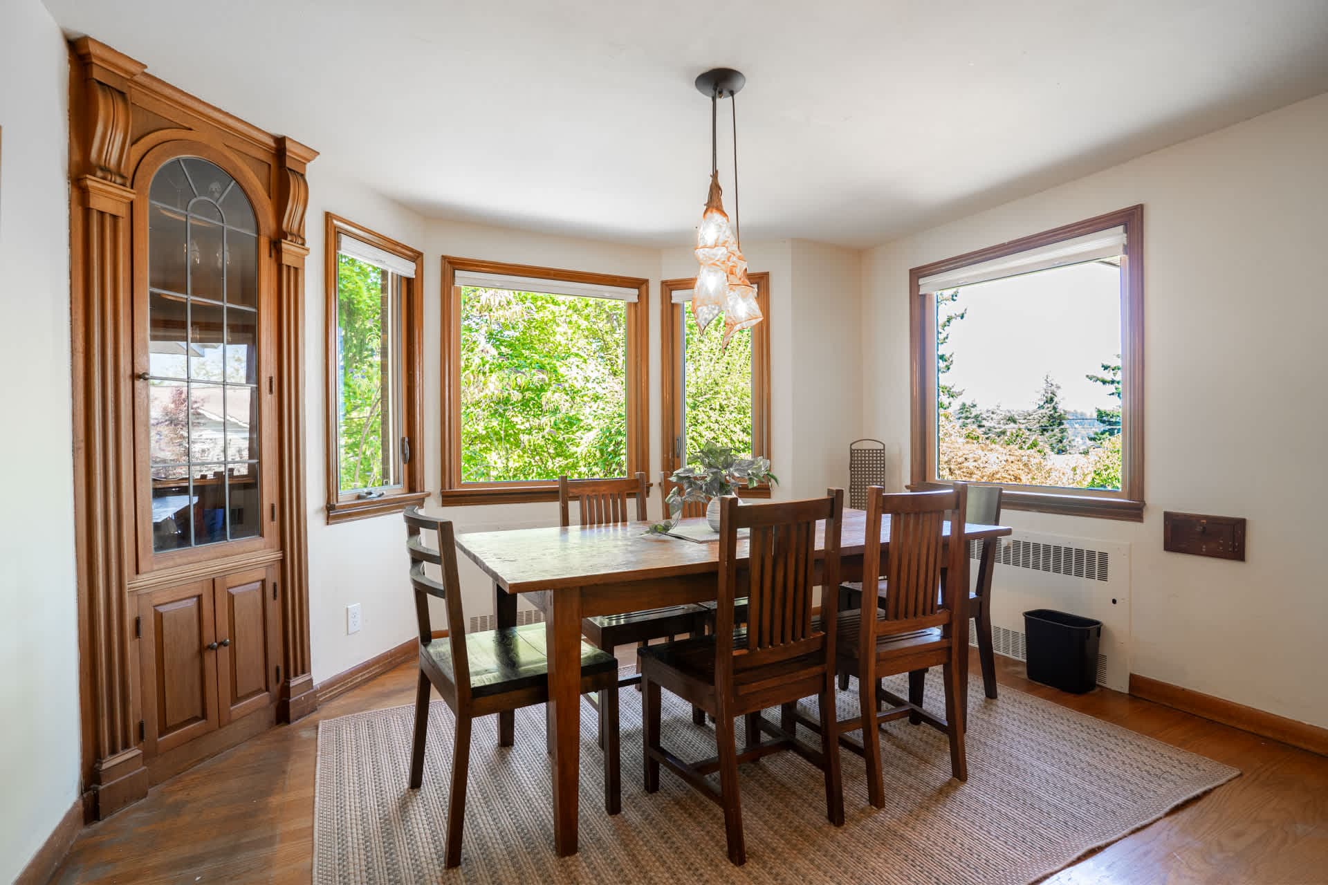 Gather around the dining table bathed in natural light, where wraparound windows frame lush greenery and distant views, creating a serene backdrop for slow breakfasts, sunset dinners, and meaningful conversation.